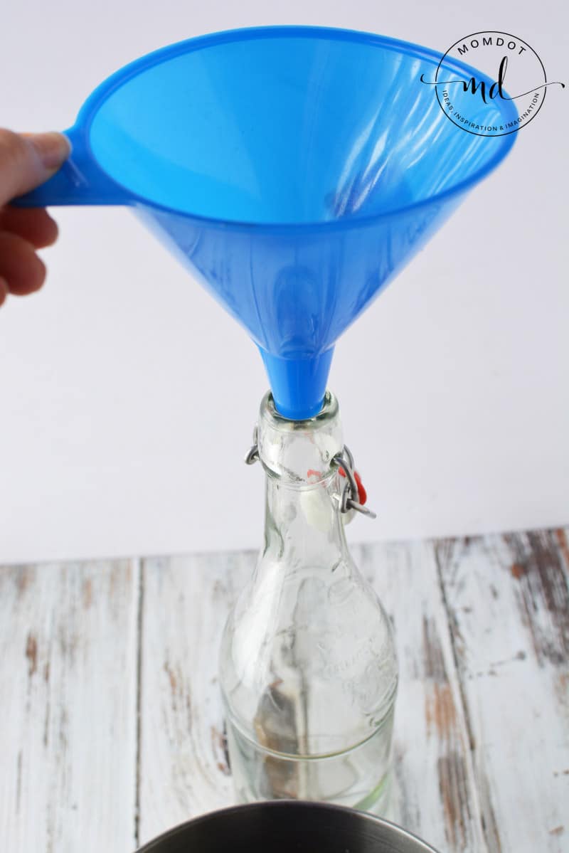 A blue funnel is used to pour the sugary coffee and vodka mixture into a bottle that can be sealed to age homemade Kahlua.