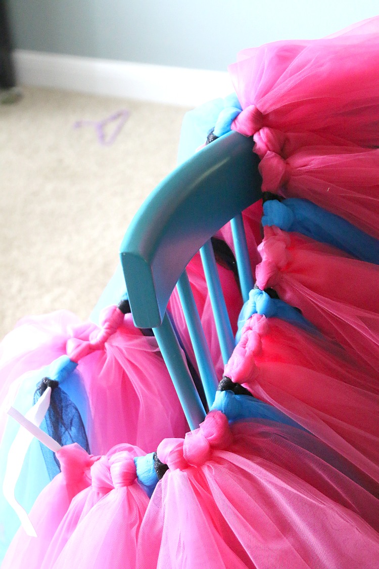 A no-sew tutu skirt looped on the back of a blue wooden chair to show how the waistband is looped with tulle strips to make the tutu skirt.