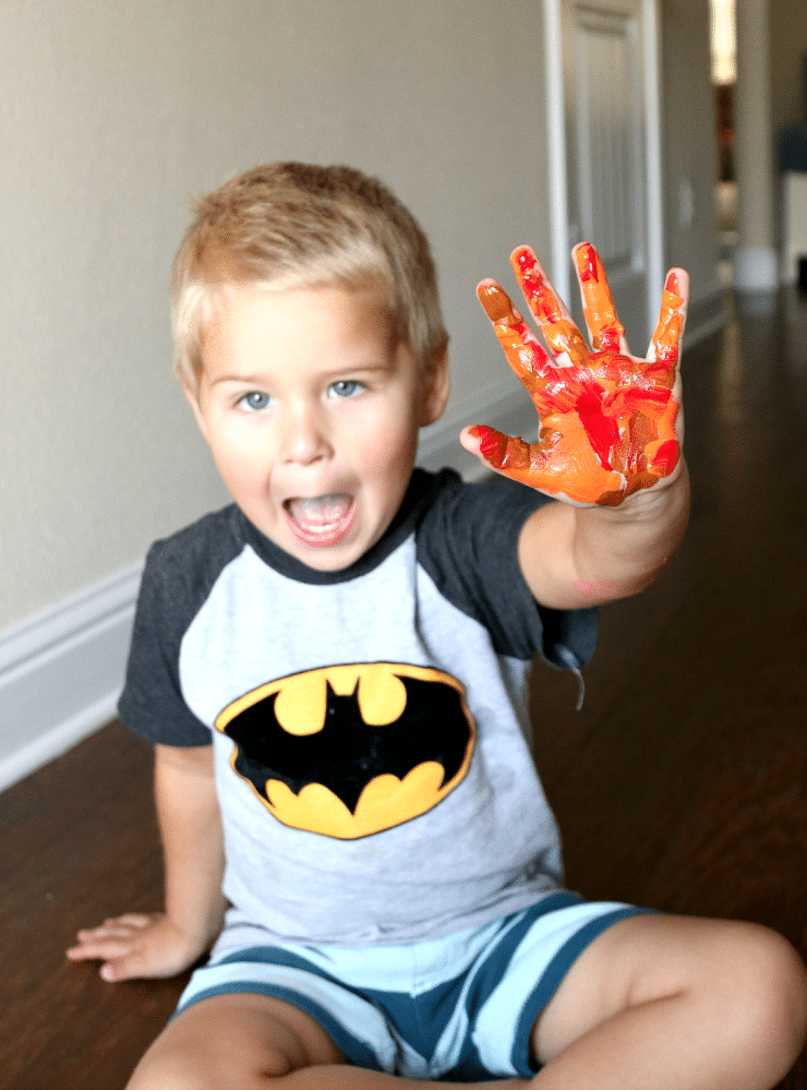 Boy with paint all over his hand in orange, brown, and red for Thanksgiving handprint craft.