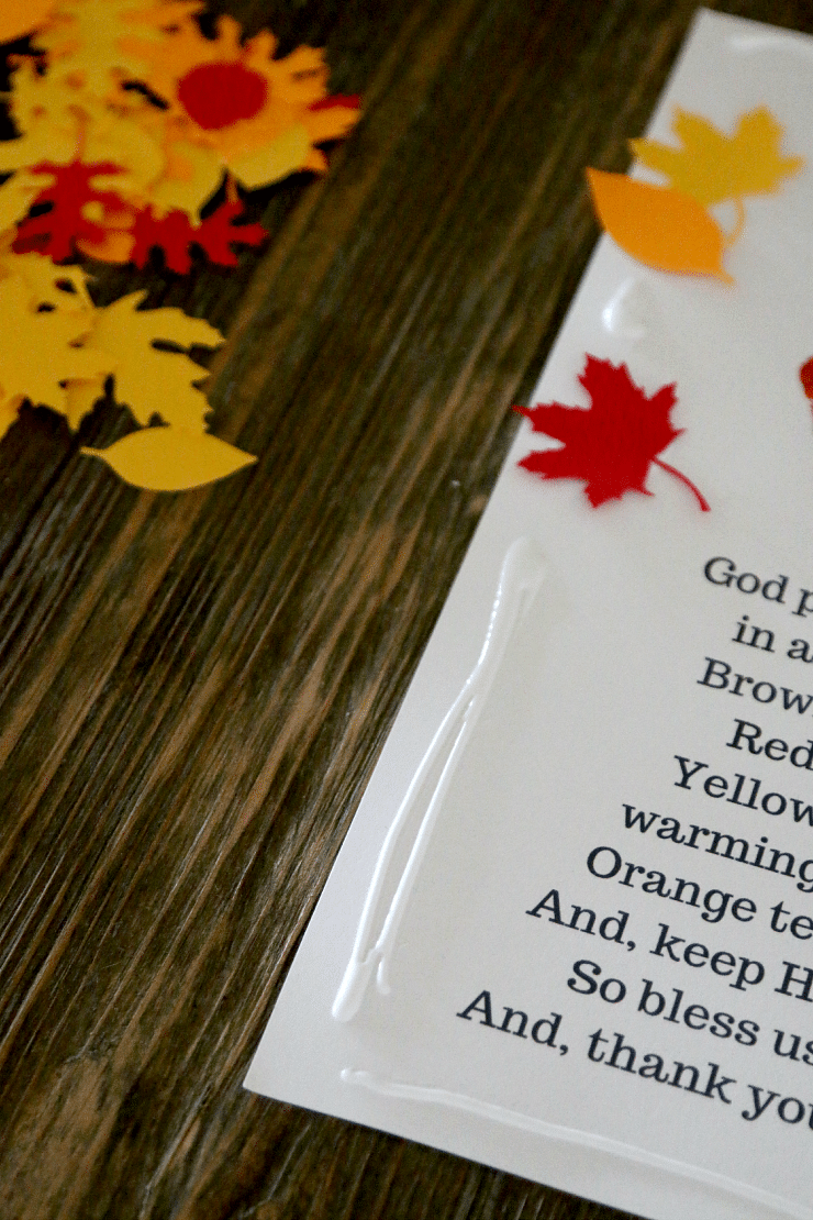 Laminated Thanksgiving handprint poem being decorated with paper fall leaf cutouts.