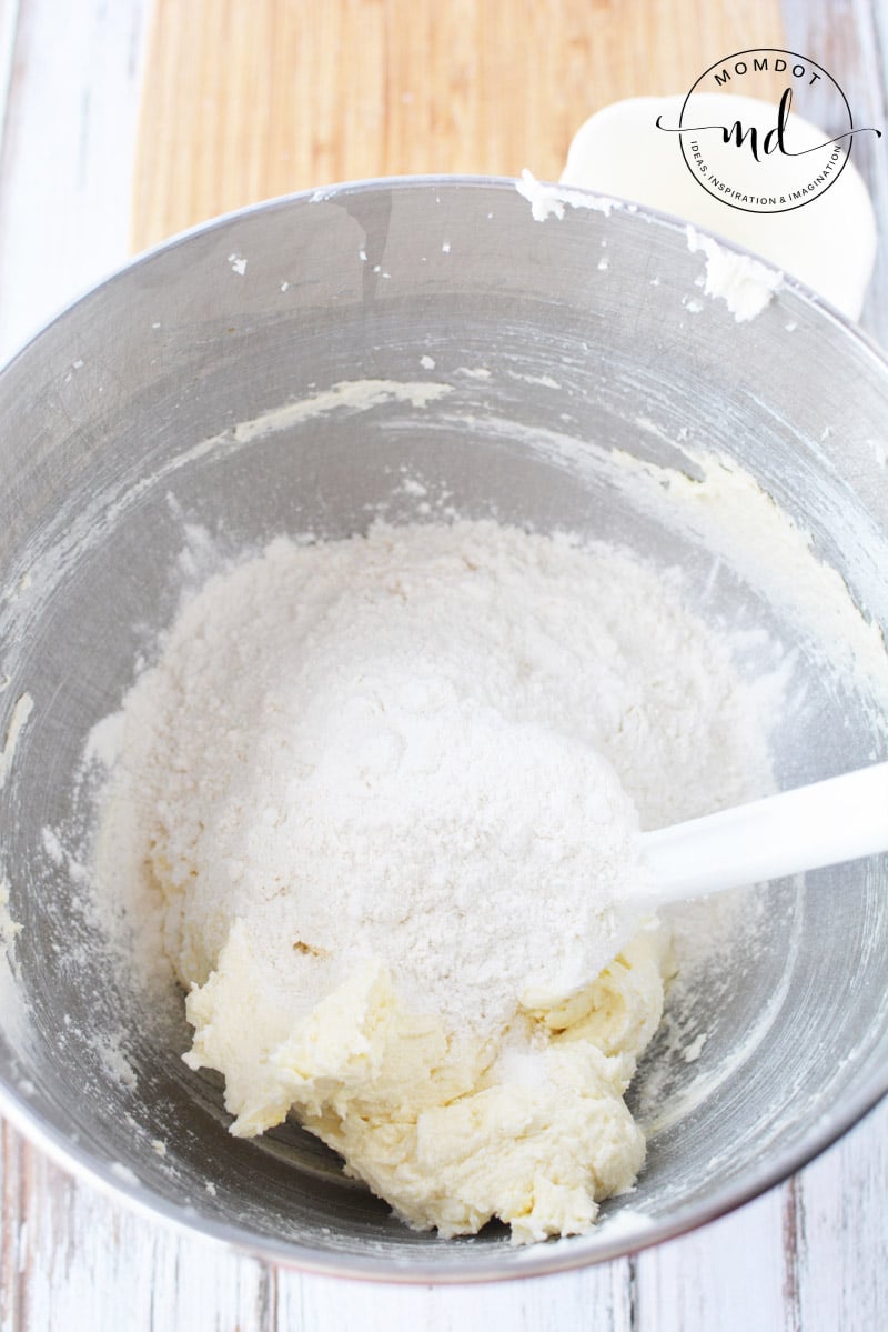 Sugar cookie batter in a bowl with flour on top to be mixed in.