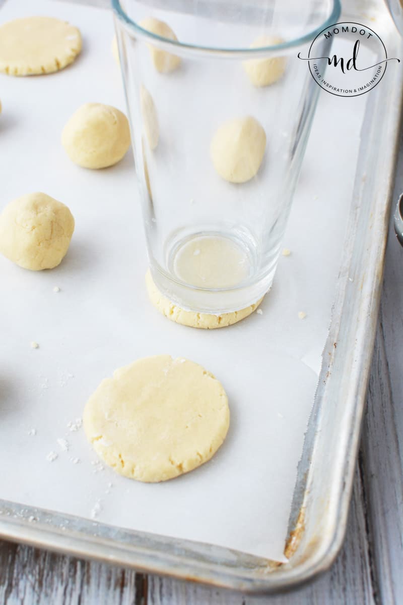 A glass being used to flatten sugar cookie dough balls into round cookie shapes.