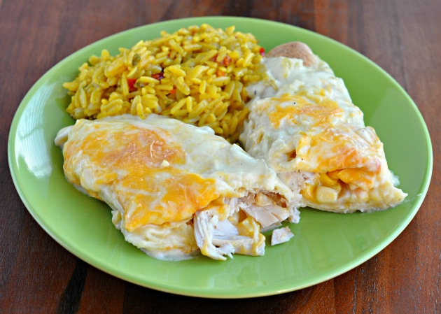 A creamy white chicken enchilada cut in half on a green plate to show creamy texture with saffron rice on the side.