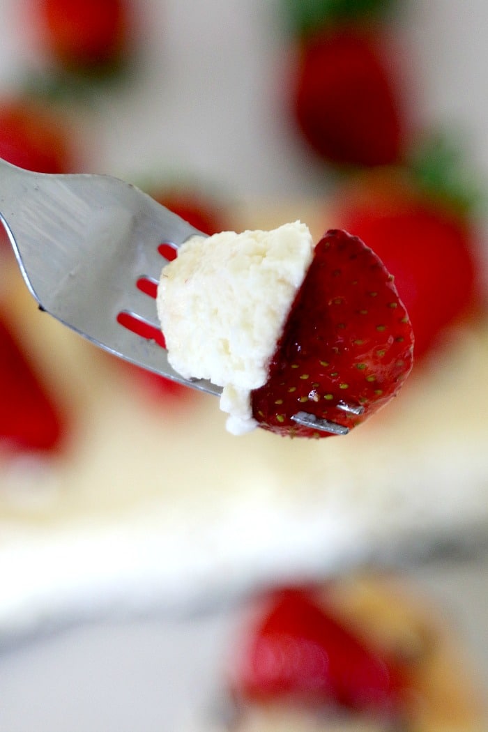 A bite of Philly cheesecake and fresh strawberry on a fork