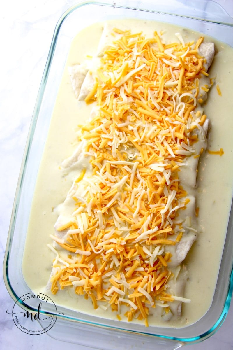White chicken enchiladas in a pan, covered with white sauce and shredded cheese, ready for baking.