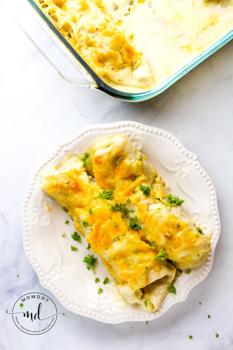 Finished white chicken enchiladas in the pan with 2 creamy white chicken enchiladas on a plate.