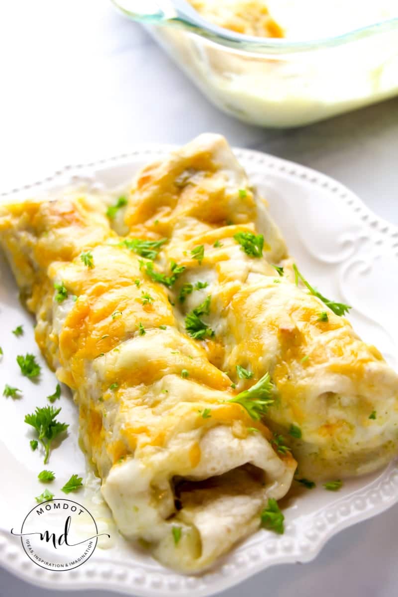 2 creamy white chicken enchiladas on a fancy white plate with parsley sprinkled on top.