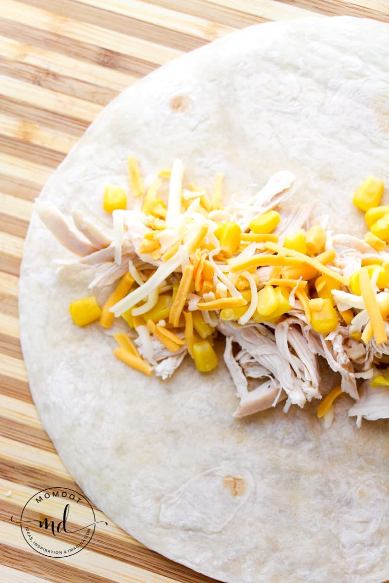 Shredded chicken, corn, and shredded cheese in a tortilla to make white chicken enchiladas.