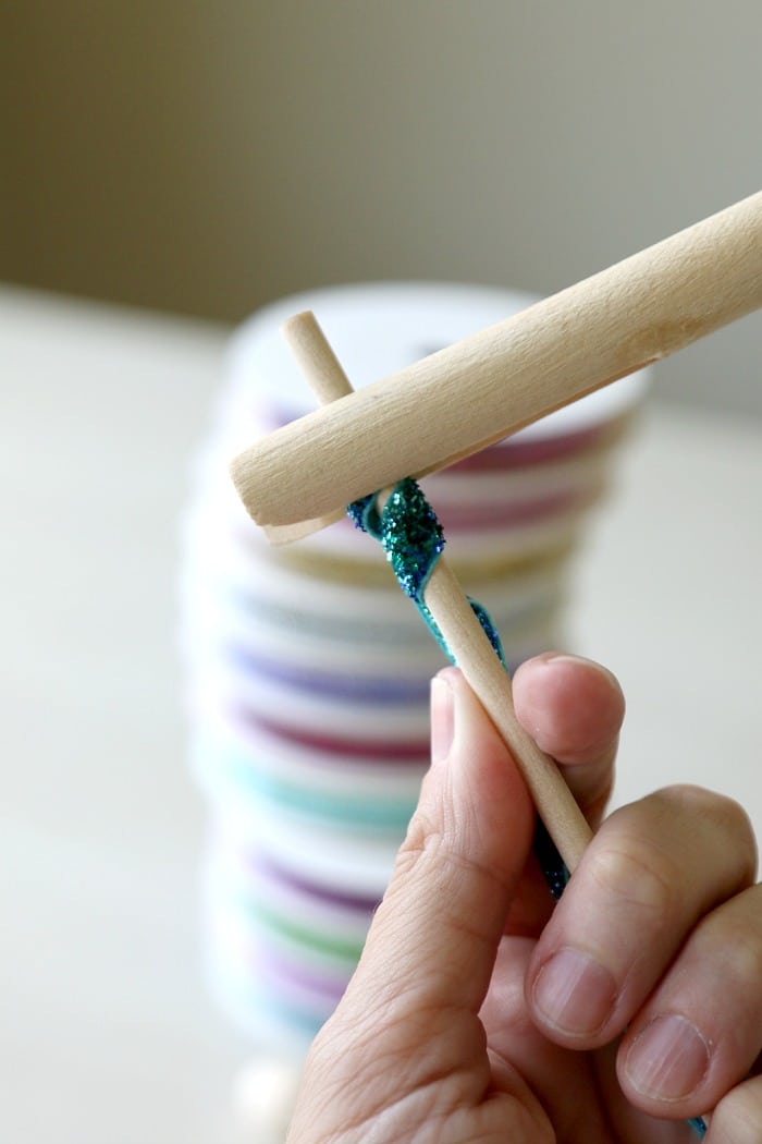 A korker ribbon is being started by using a clothespin to attach the ribbon to a wooden dowel.