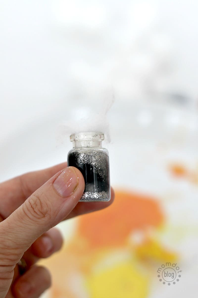 An element jar necklace representing the moon or night sky is made with silver glitter inside the jar that's covered with black painted cotton balls.