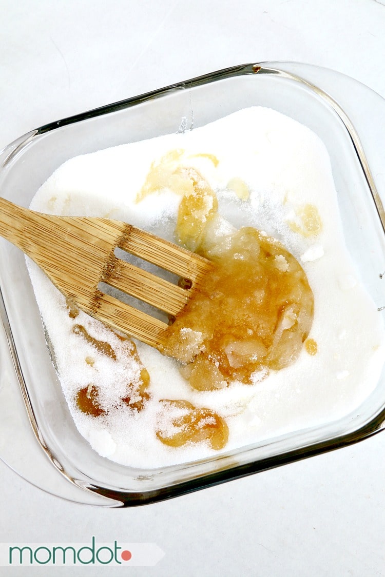 A bamboo spoon stirring hard candy ingredients in a microwavable casserole dish.