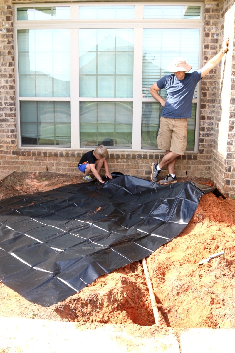 Father and son placing a black pond liner inside the hole dug for a new pond.