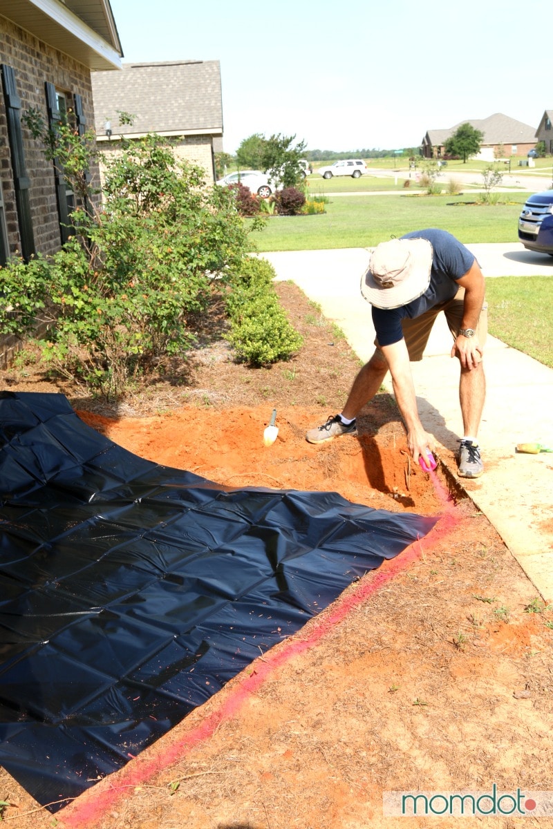 Man using pink spray paint to mark the edge of a new pond before placing liner.