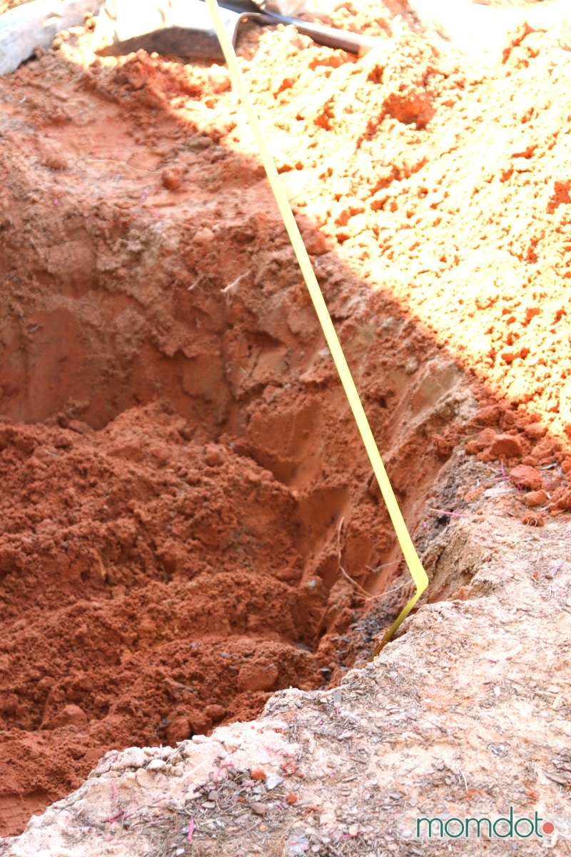 Measuring tape inside a hole for a new pond, making sure it's 12 inches deep all around.