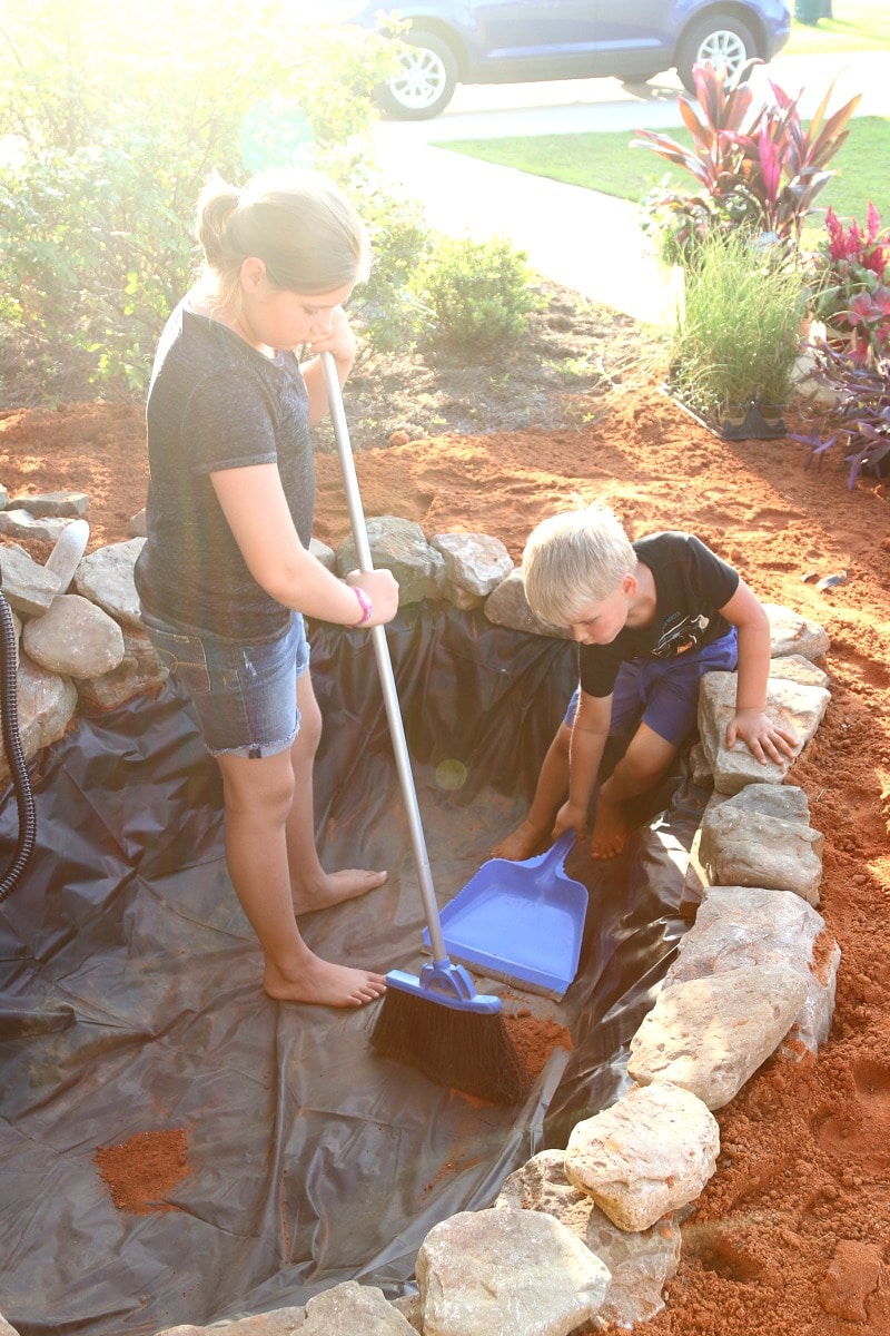 Children sweeping dirt from the inside of the pond liner so it can be filled with fresh water
