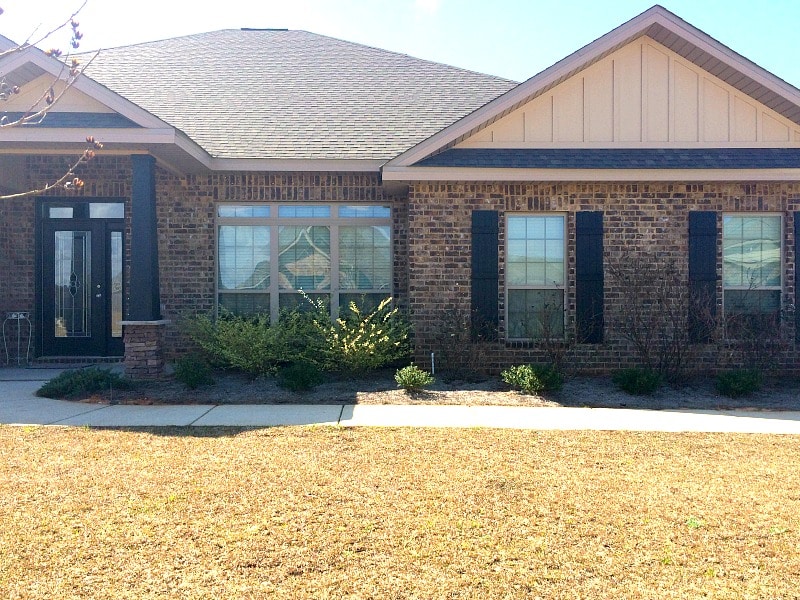 Front of a beautiful brick home with shrubs and a yellowed lawn