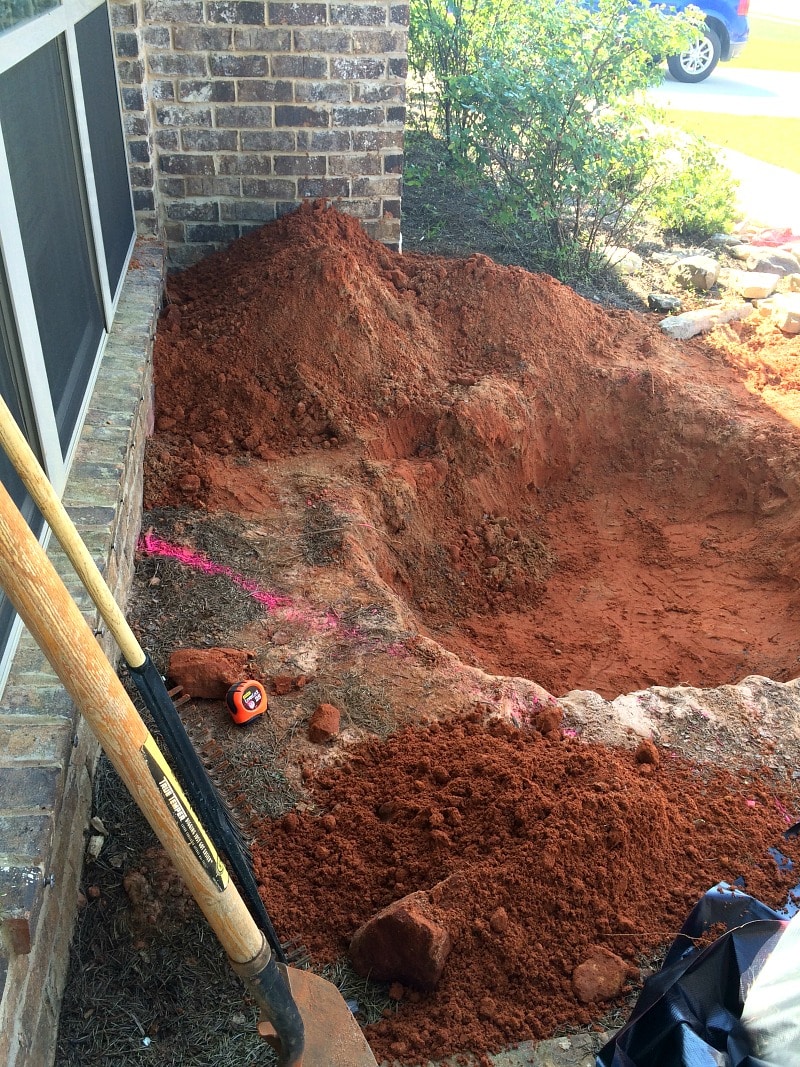 Shovel and rake leaning against the wall of the house with a new hole dug for a pond