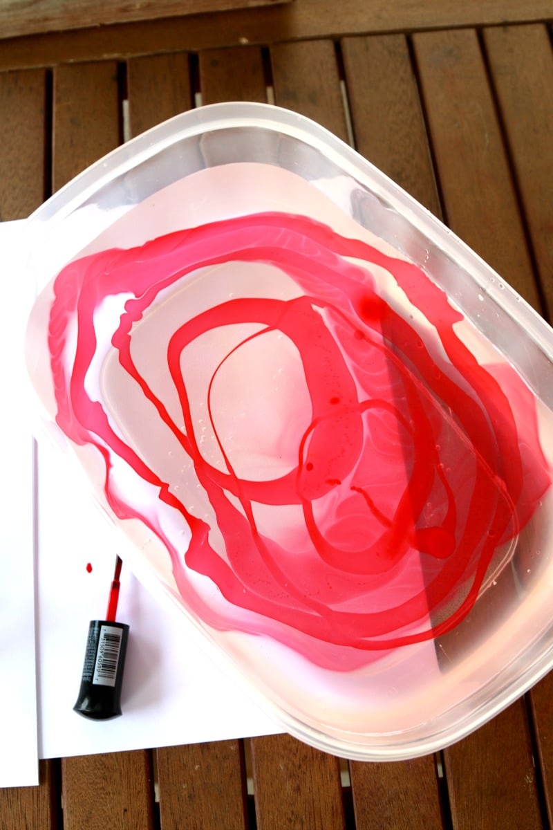 A disposable container with water in it and red nail polish floating on top to make a pattern for marble dipping.