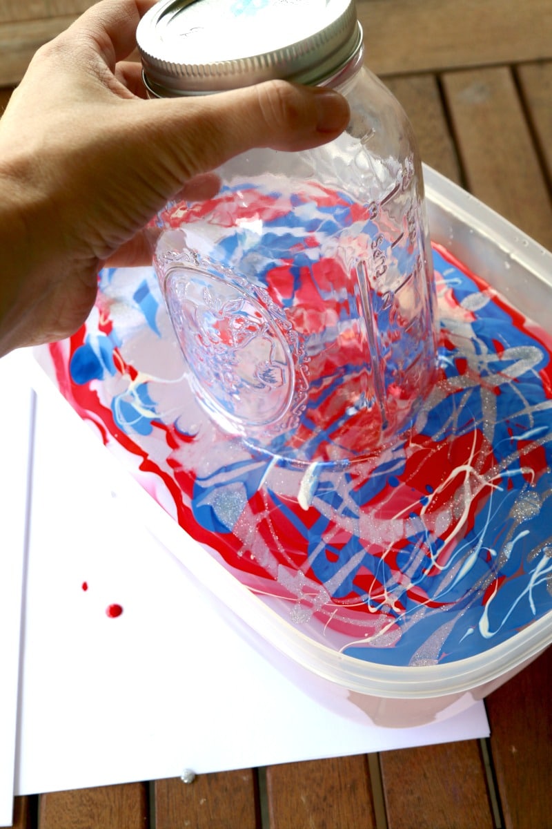 A mason jar being dipped into nail polish colors that are floating on top of water to make a marble dip mason jar.
