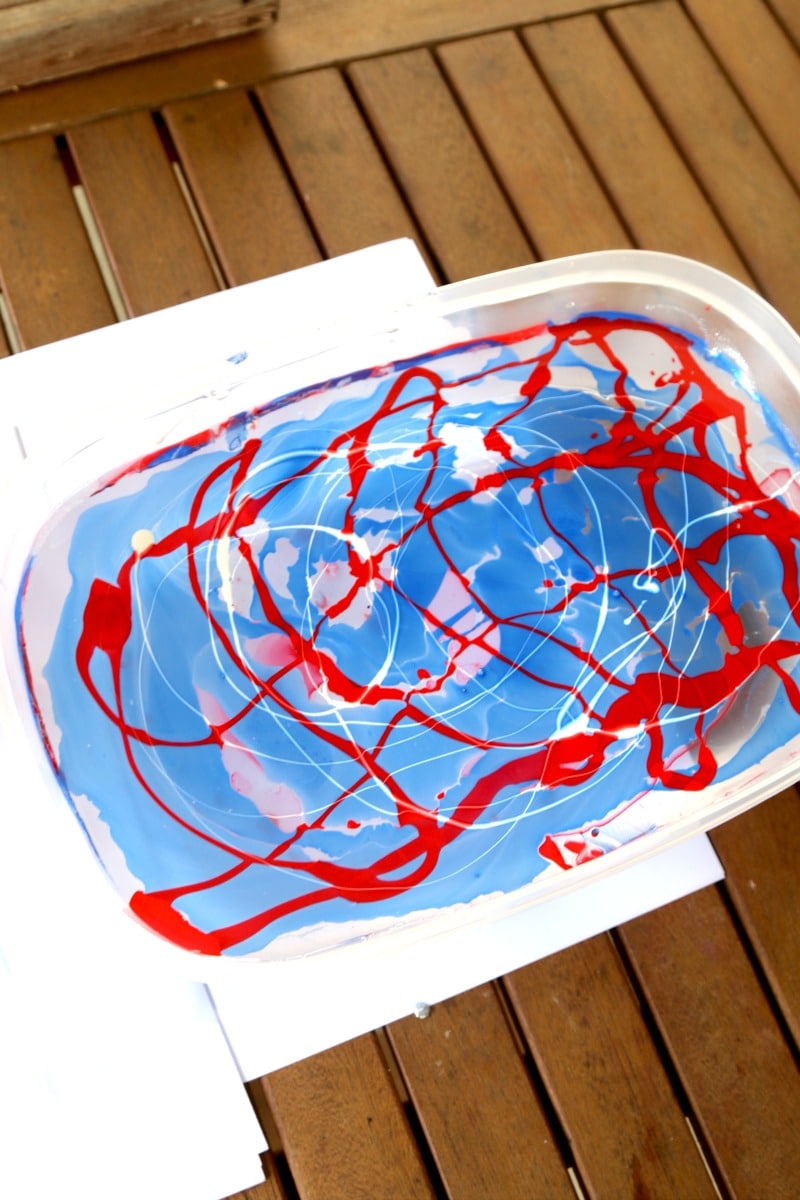 Red and blue nail polish floating in water for marble dipping a mason jar.