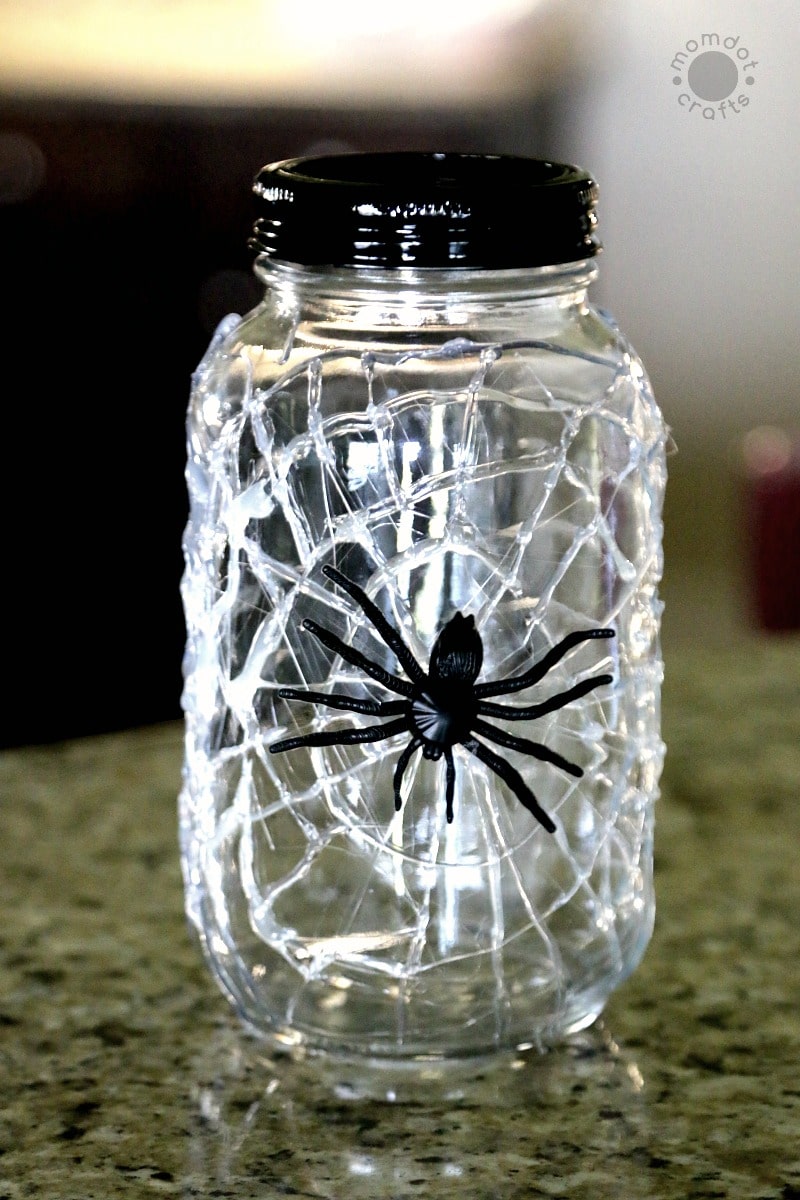 Spider web design on a mason jar with a large fake spider on the outside for a Halloween decoration