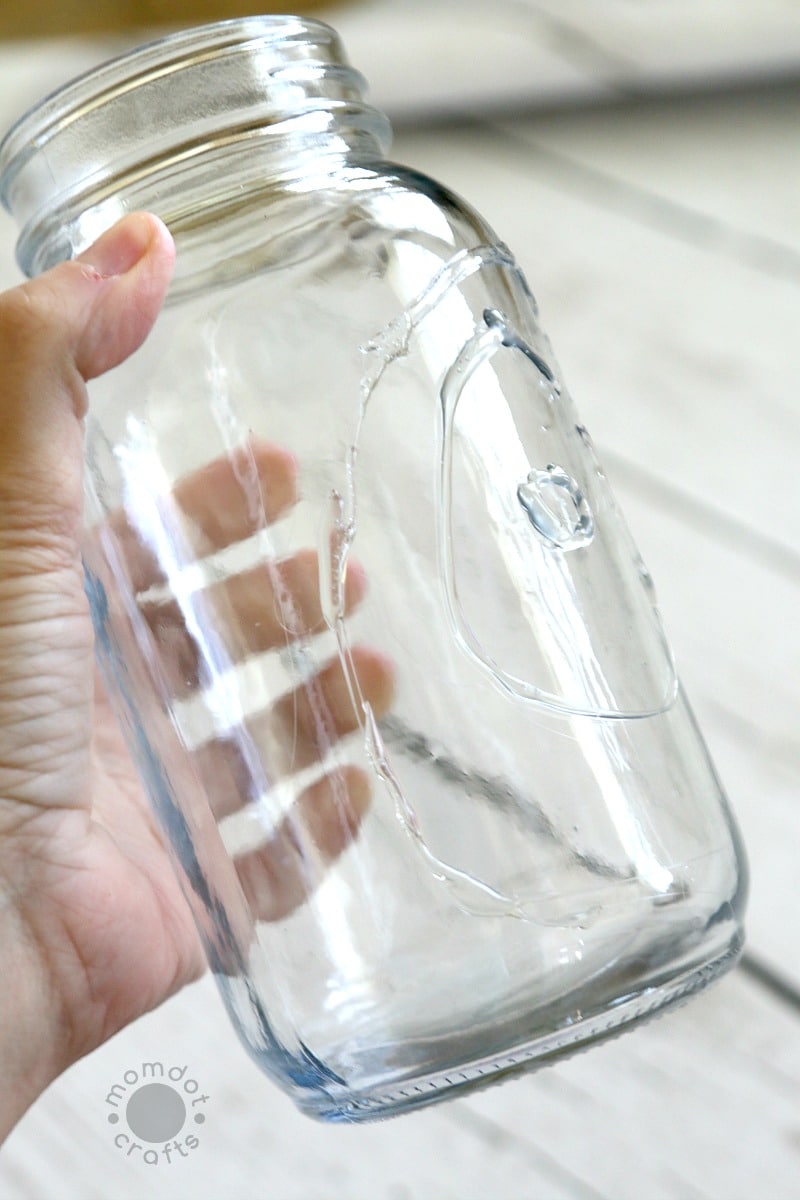 Mason jar with circles of hot glue that are the start of a web for a Halloween decoration