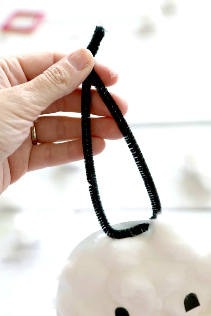 A black pipe cleaner threaded through a hole punched in the top of a cotton ball ghost to hang it up