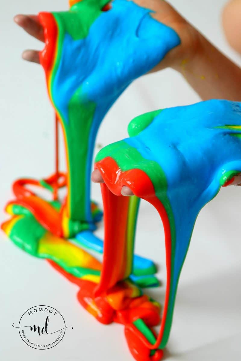 DIY rainbow slime recipe dripping off of hands showing the bright blue, green, red, and yellow colors.