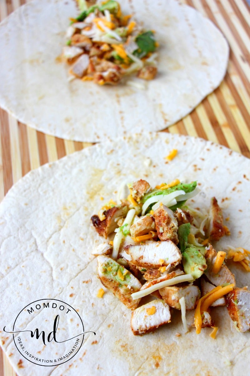 Tortilla with chicken, cilantro, shredded cheese, and avocado mixture in the middle.