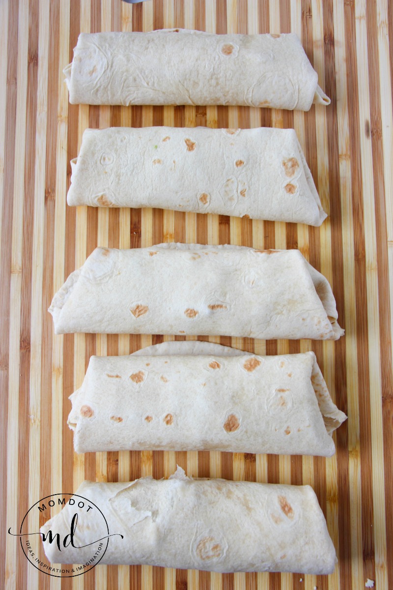 5 Chicken Avocado Burritos on a cutting board, ready to brown in a hot skillet for a crispy finish on the outside.