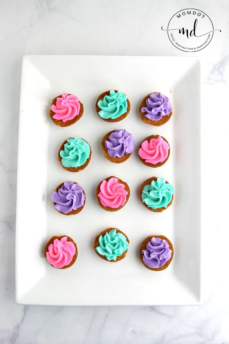 Nilla wafers on a plate with pink, green, or purple frosting swirled in the middle, for making shell cookies
