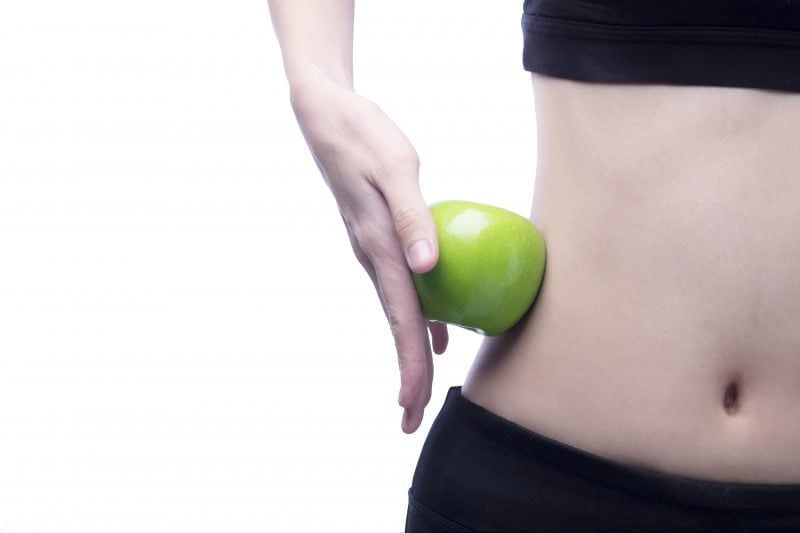 A woman holding a green apple to her trim waist