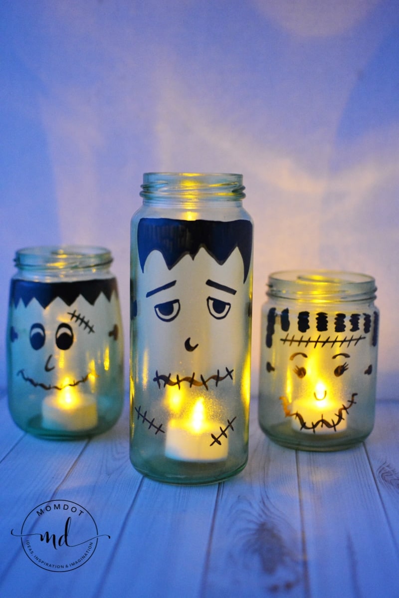 Halloween mason jar luminaries have monster faces painted on the outside and a flameless tea light inside