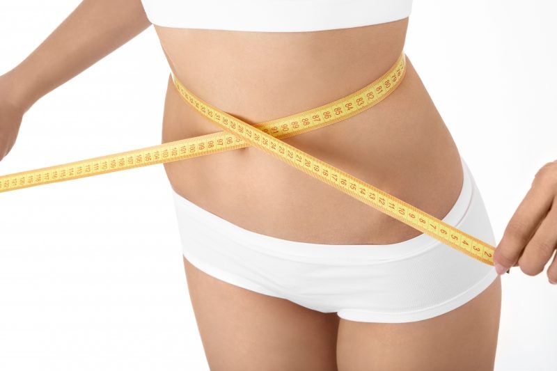 A thin woman holding a fabric measuring tape around her waist