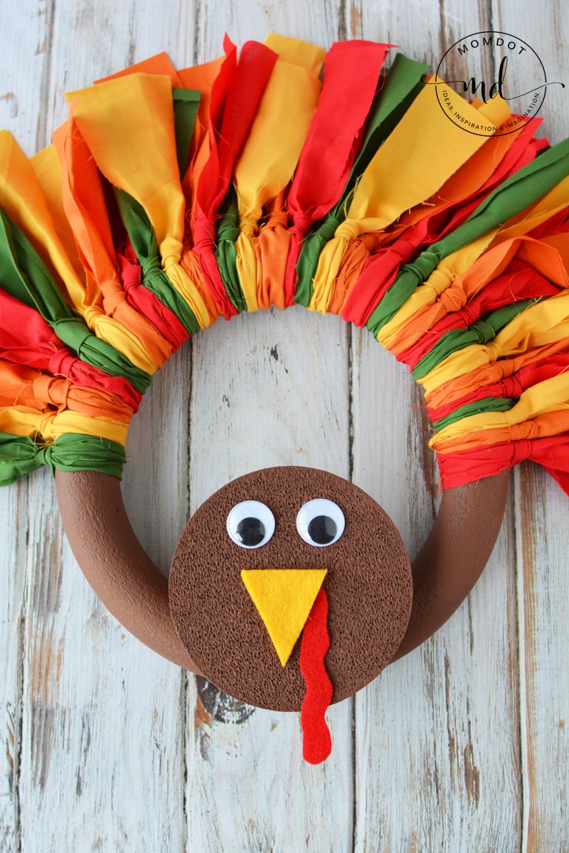 Tom the Turkey wreath made with red, yellow, and orange strips of fabric with googly eyes and a felt beak and wattle.