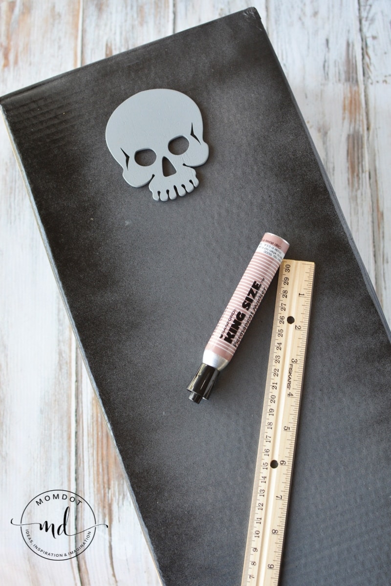 A wooden skull cutout, permanent marker, and ruler for decorating a DIY Halloween tombstone