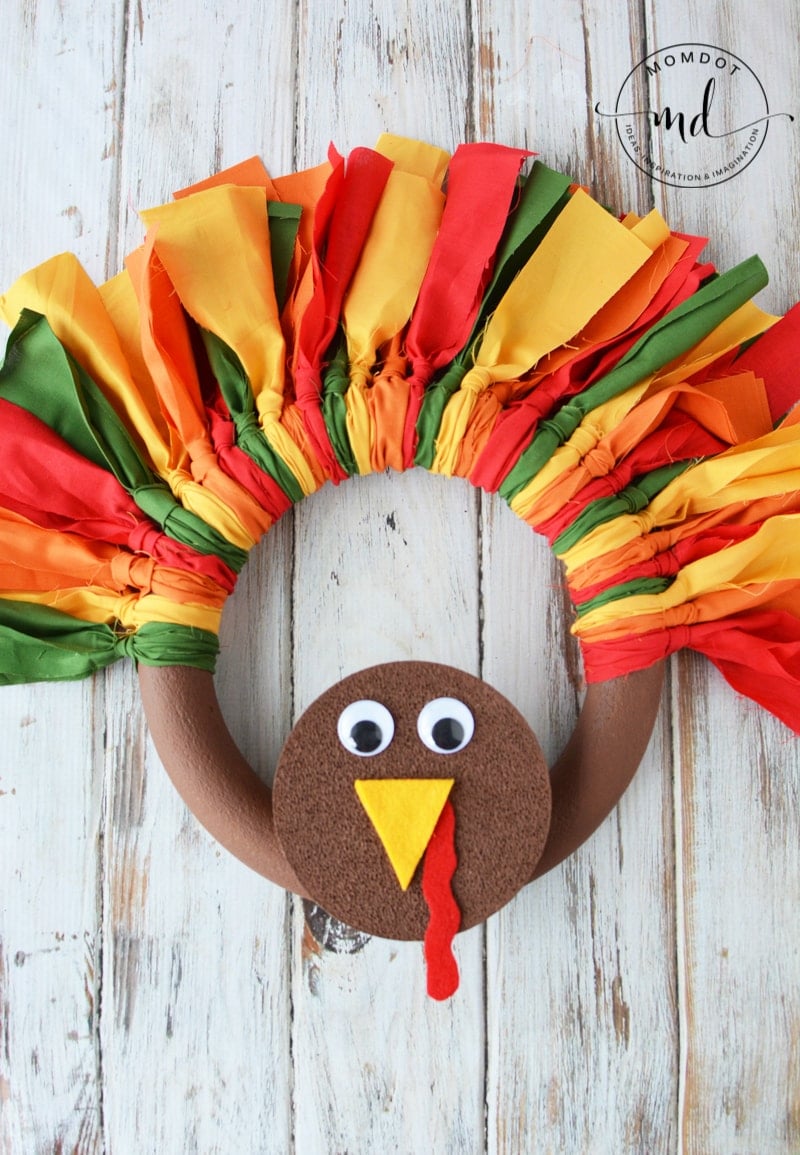 A finished DIY turkey wreath with a tail made of fabric strips and a face with googly eyes and a felt beak and snood.