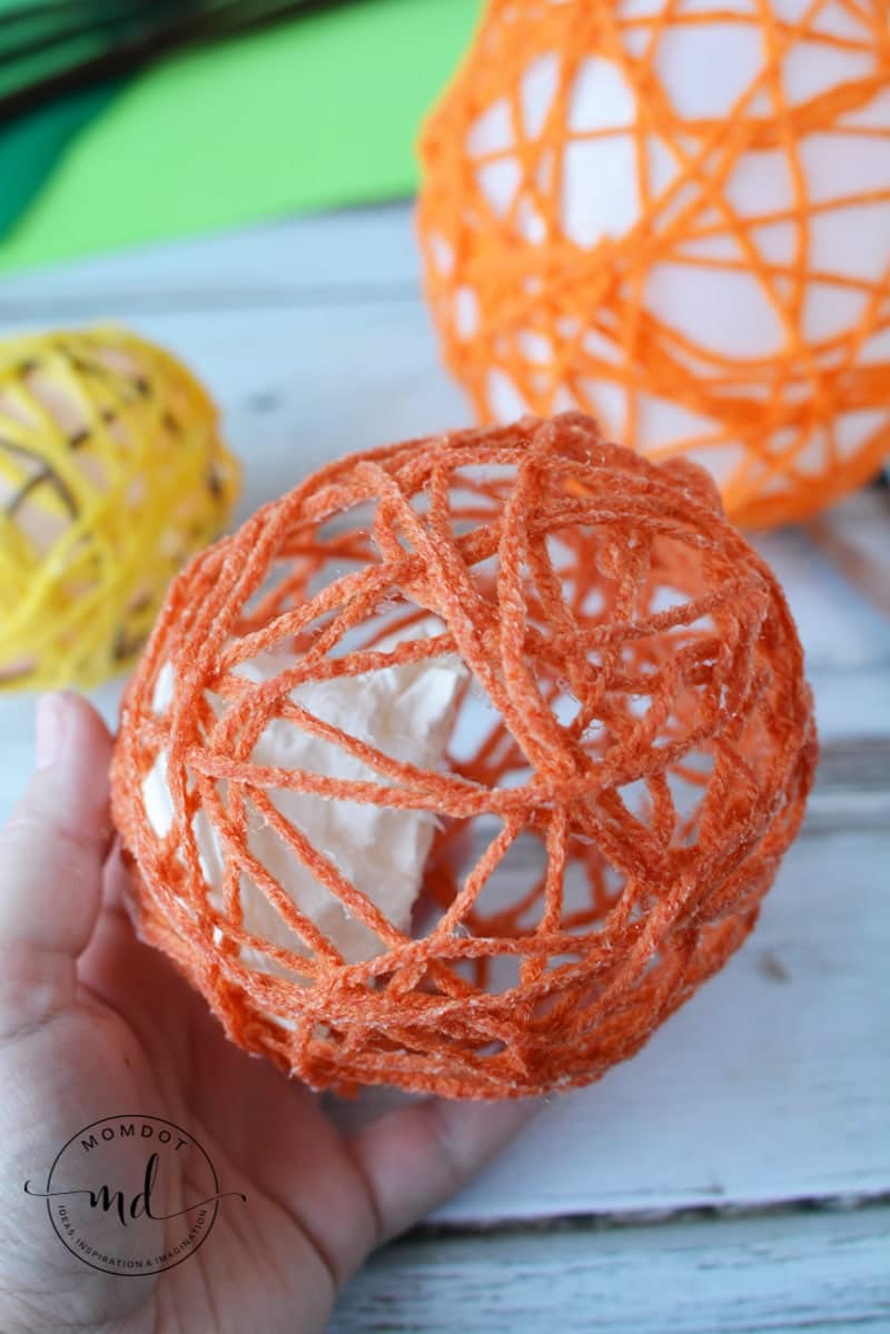 A dried orange yarn balloon with popped balloon inside.
