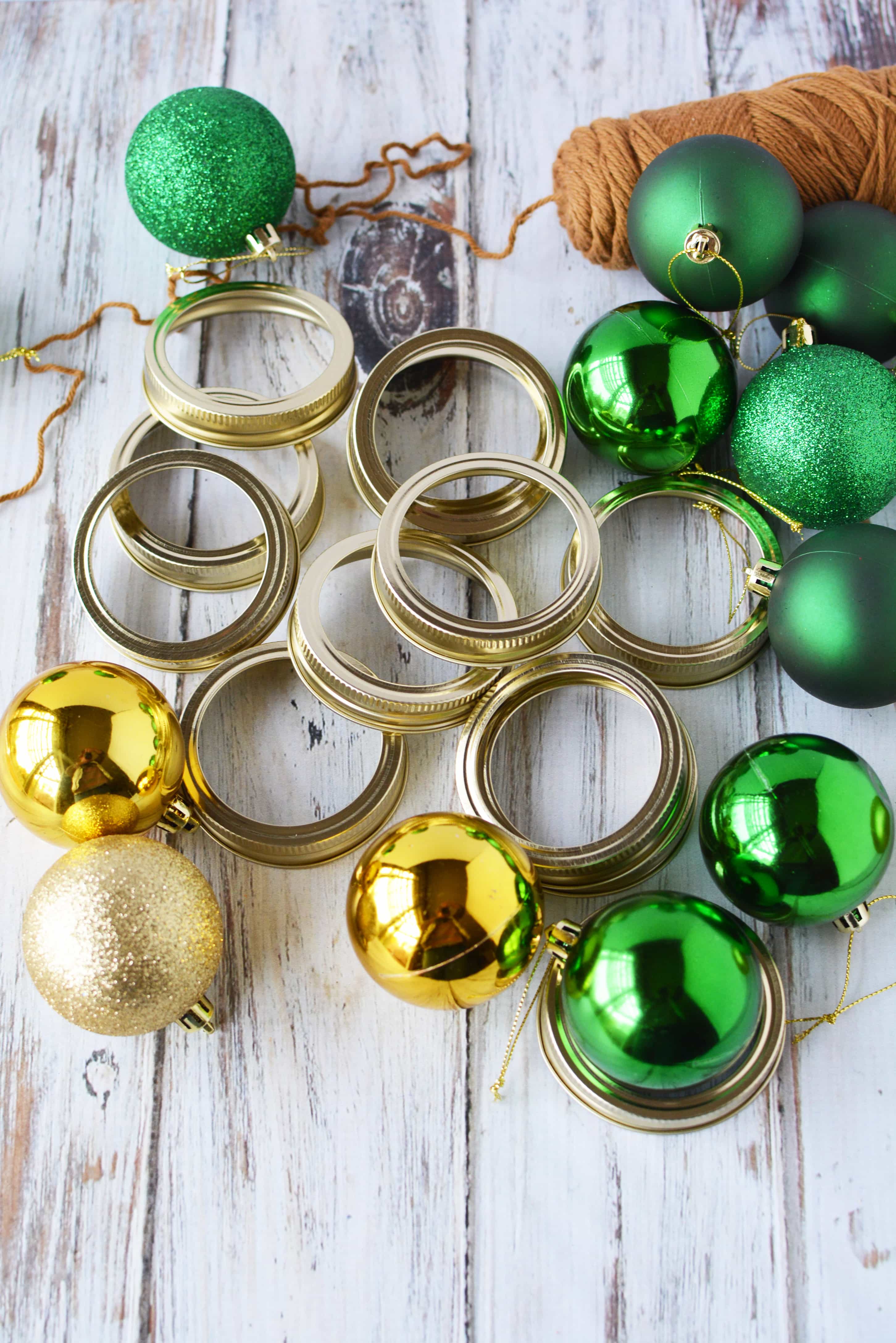 Mason jar lid bands on a table with brown yarn and green and gold plastic tree ornaments to make a mason jar lid Christmas tree.