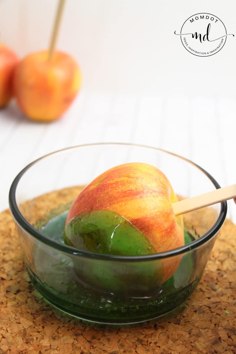 An apple being dipped in a bowl of melted Jolly Ranchers to make candy apples