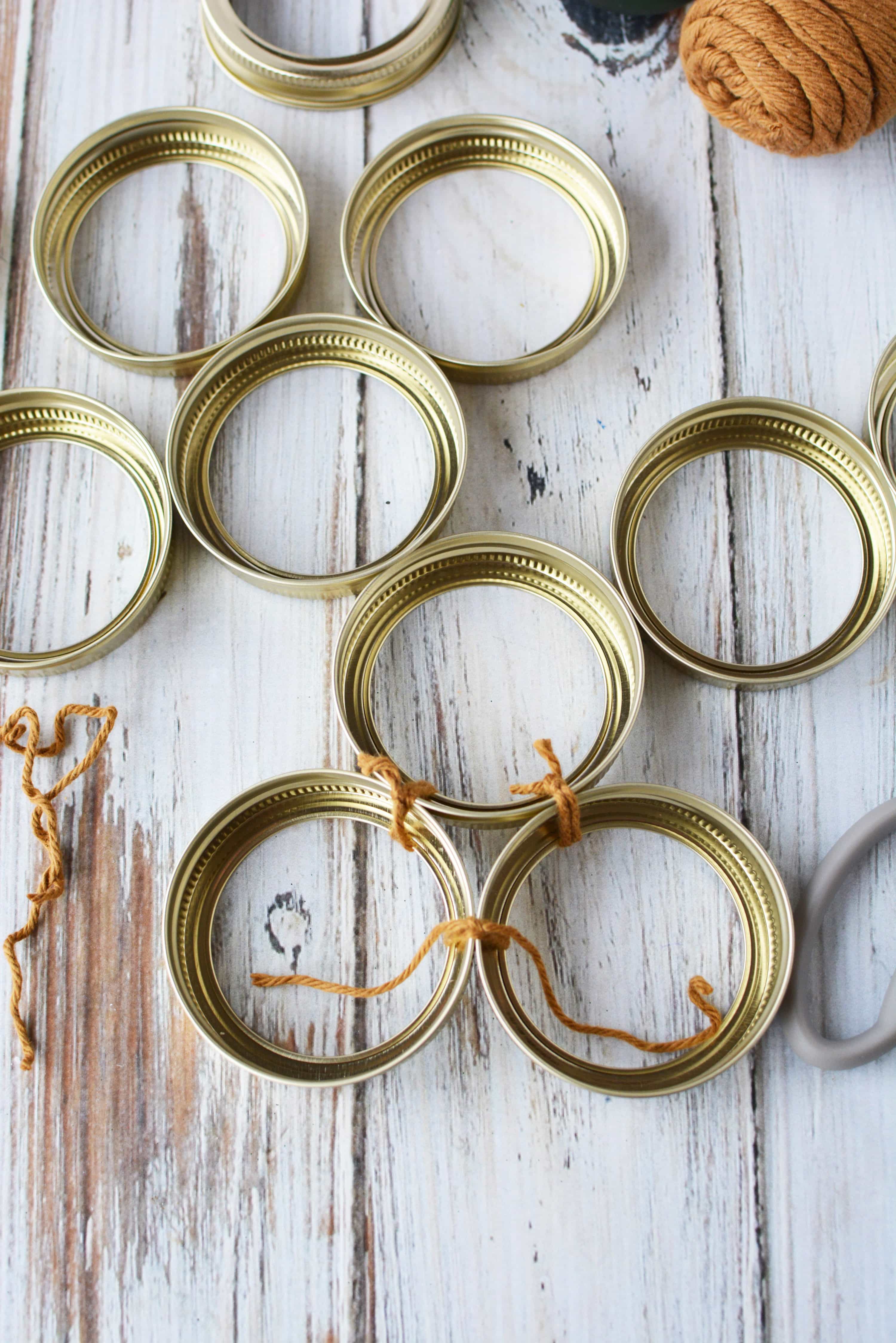 Mason jar lid bands tied together with brown yarn to begin a tree shaped Christmas decoration.