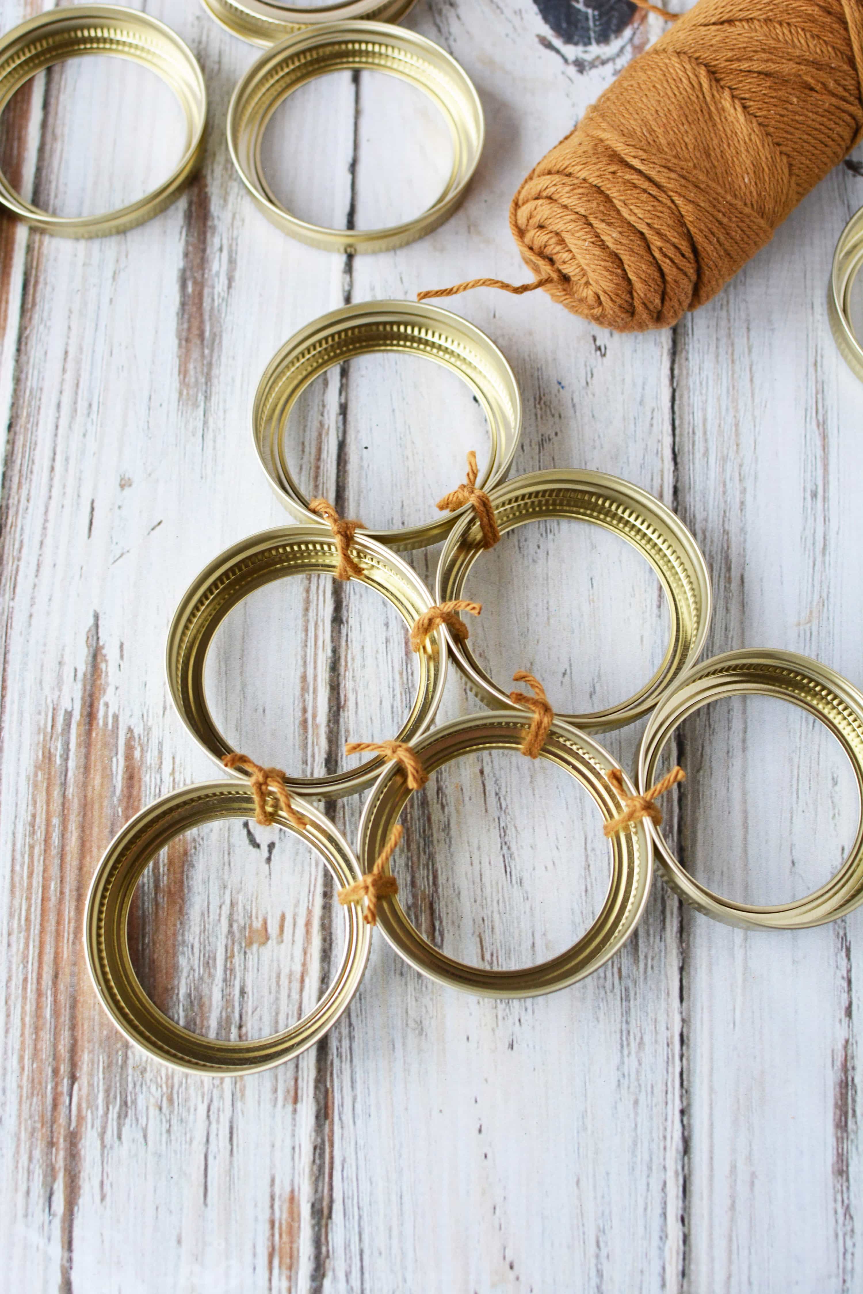 6 mason jar lid rings tied together in a triangle shape with brown yarn to make the shape of a Christmas tree wreath.