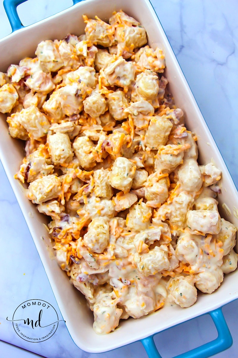 Tater tot casserole with cream of chicken soup in a casserole and ready to go in the oven.