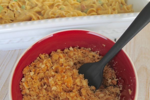 A casserole with tuna noodle mixture in it, and a spoon mixing Ritz crackers with melted butter