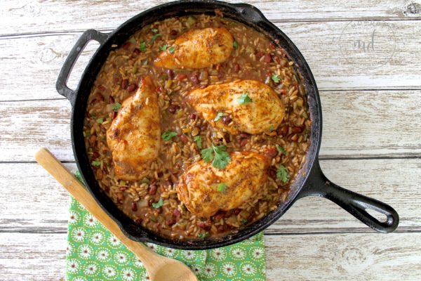 A cast iron skillet with red beans and rice and chicken in it and a wooden spoon on the side.