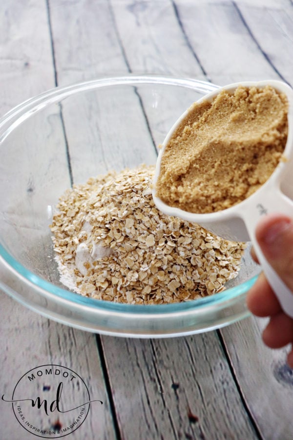 Brown sugar being added to a bowl of apple crisp topping ingredients.