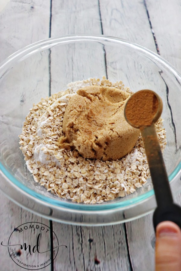 Cinnamon being added to a bowl of other ingredients to make apple crisp topping.