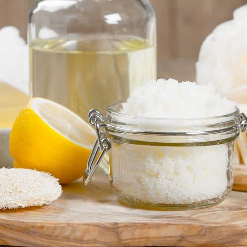 A half of a lemon and a small jar of a homemade gift for mom of lemon sugar scrub that's a luxurious bath time exfoliant.