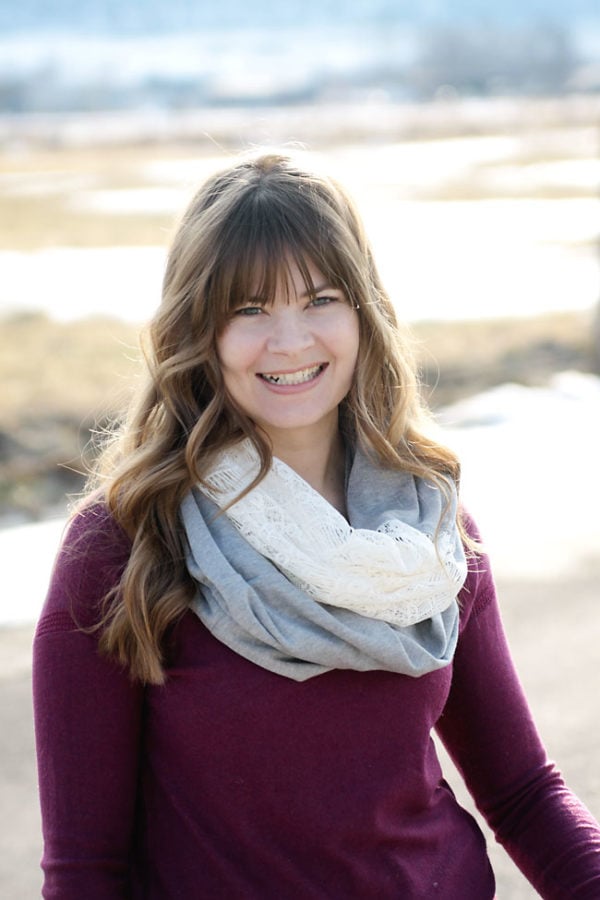 A woman wearing a maroon sweater and a gray infinity scarf with a lace insert that makes it look so feminine.