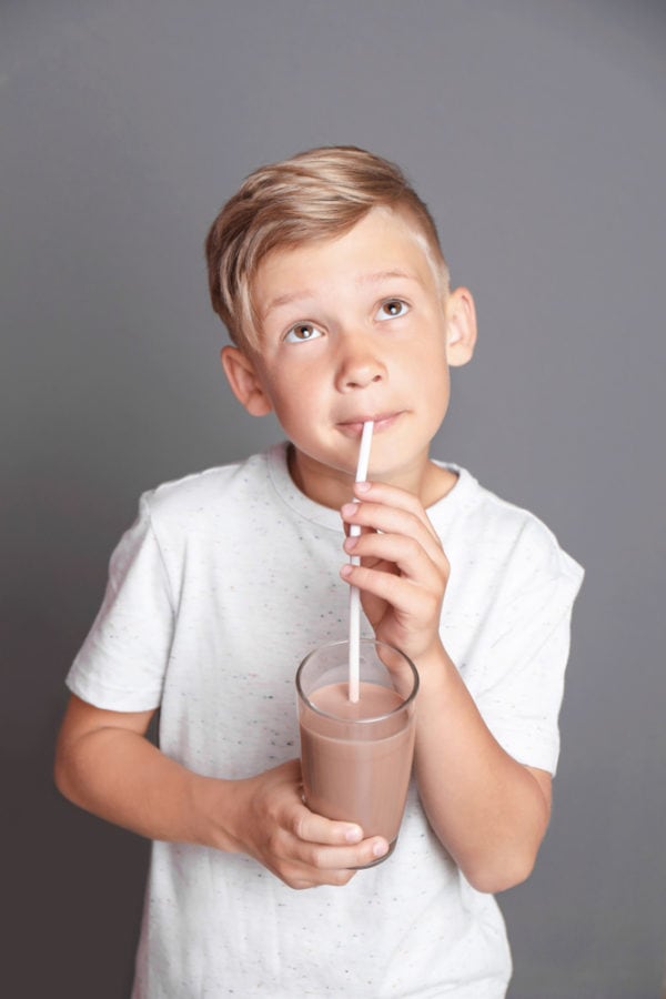 Boy enjoying a glass of chocolate protein powder drink with a straw